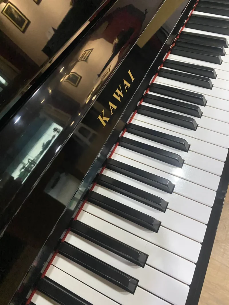 Upright piano Kawai K18E dengan finishing hitam glossy, desain minimalis, dan kualitas suara hangat serta seimbang untuk latihan dan penggunaan harian.